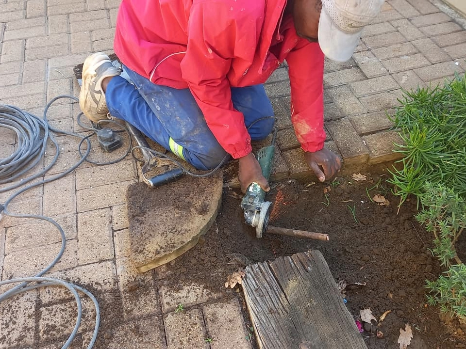 a professional plumbre using an angle grinder to cut a copper pipe in the ground