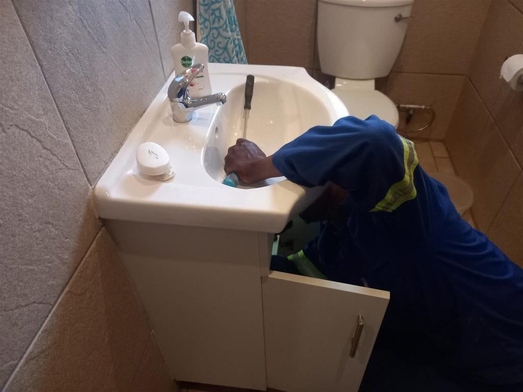 Plumber installing a basin waste and drain fitting under a bathroom vanity sink