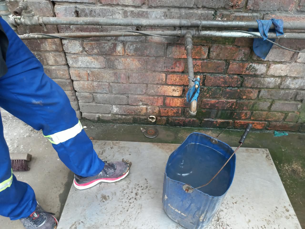 Plumber repairing a leaking outdoor pipe joint against a brick wall